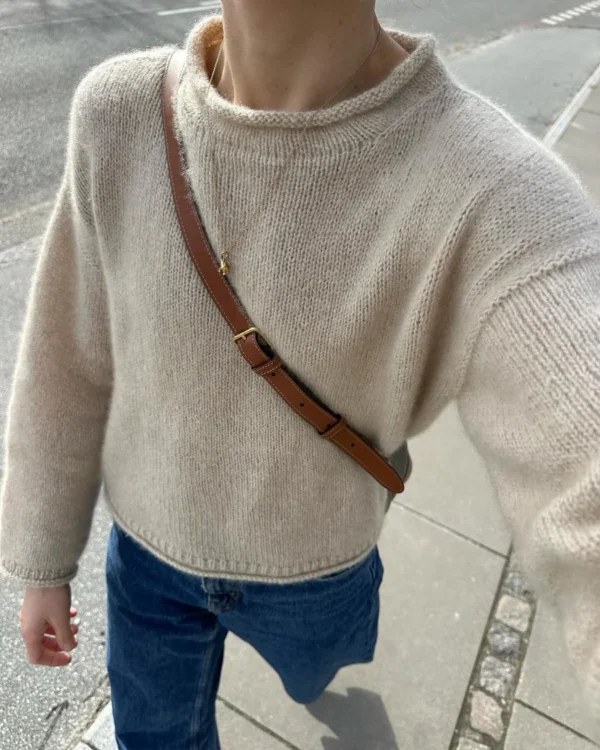 En person rusler langs fortauet, iført en Cloud-bluse som passer perfekt til de blå jeansene deres og den brune crossbody-remmen.