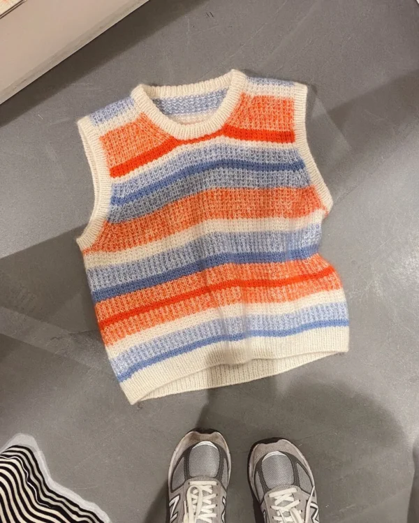 En livlig fredagsslipover med oransje, blå, hvite og korallstriper ligger på gulvet sammen med et par grå joggesko. Perfekt for lagdeling, dette ensemblet fremkaller en koselig stemning.