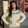 En kvinne med langt krøllete hår står utendørs, iført en Hjertegenser voksen XXL-genser med hjertemønster og jeans. Selvsikkert poserer hun med hendene på hoftene foran en bygning.