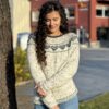 En kvinne med langt krøllete hår, iført en Hjertegenser voksen XXL-mønstret genser og jeans, står ved siden av et tre på en solskinnsdag.