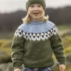 Et barn i strikket genser og matchende lue fra "Flokken"-kolleksjonen, med nordiske mønstre, står ute og stråler av glede, som om hver maske gjenspeiler familiens lykke.