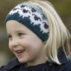 Et barn fra «Flokken» til hele familien ses iført et blått pannebånd med hvitt og svart mønster, smilende mens de ser til siden mot en uskarp grønn bakgrunn.
