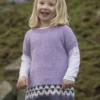 Et lite barn, en del av «Flokken»-familiekolleksjonen, smiler utendørs mot en gresskledd bakgrunn iført en lys lilla strikkekjole over en hvit langermet skjorte.