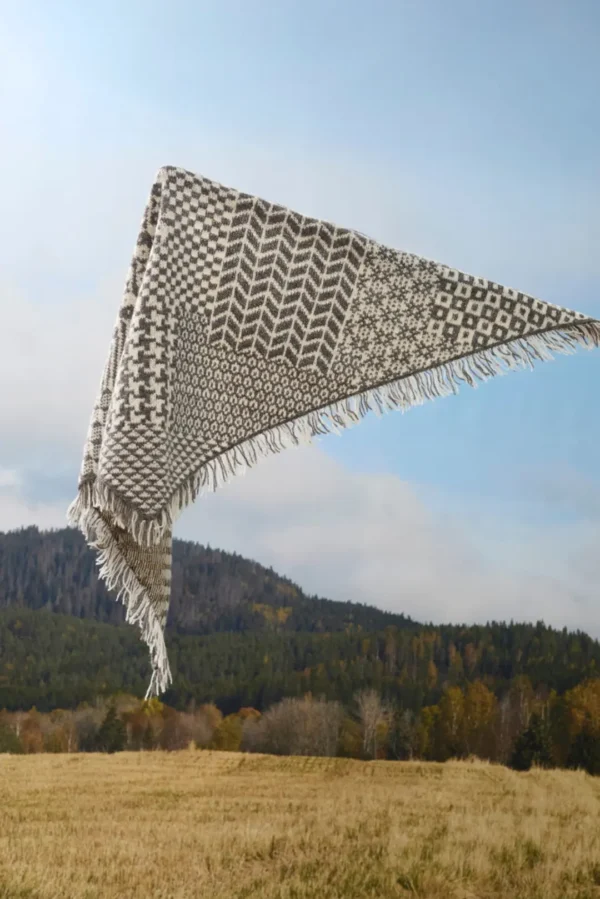 Et 455 Nordisk miks skjerf i grått og hvitt med frynser flyter uanstrengt mot et bakteppe av bølgende åser og klar himmel.