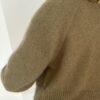Mot en sterk hvit bakgrunn bærer en person som er delvis vendt bort fra kameraet den teksturerte grønne «Darcy Cardigan», som minner om Austens klassiske stil.