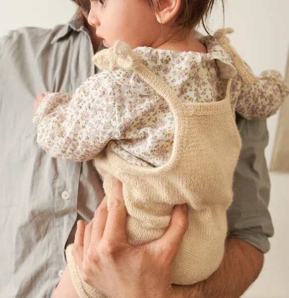 En voksen holder et lite barn iført 2505-02 Bunny shorts baby og en blomsterskjorte. Den voksnes hånd støtter barnet, som ser bort fra kameraet.