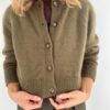 Ved å kanalisere en Jane Austen-karakter, bærer personen en olivengrønn Darcy-cardigan over en brun topp, og justerer falden med forsiktighet.