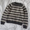The Key sweater man er en stilig grå- og hvitstripet herregenser med lange ermer, elegant utstilt på en uberørt hvit overflate.
