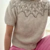 Person sittende i en trapp, iført en beige Sommer Ella 3 XL-genser med et blondemønster av blader og rosa bukser. Ansiktet er delvis utenfor bildet.