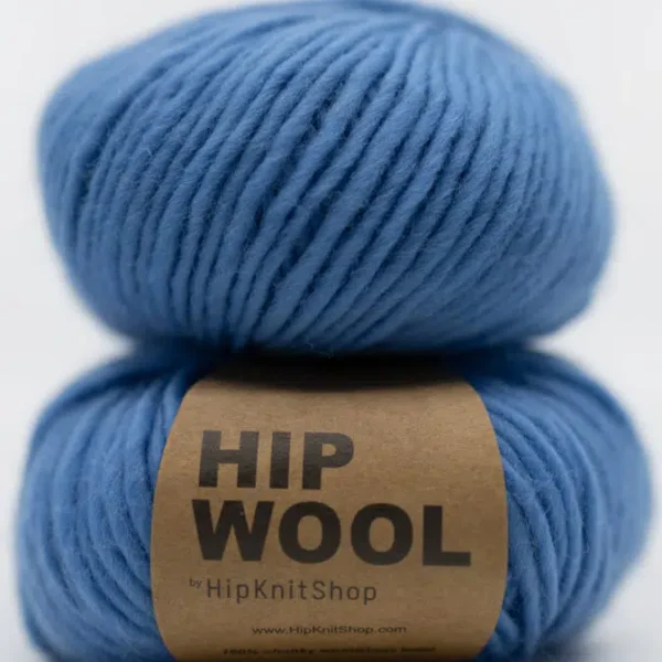 To nøster med blått Hip Wool-garn stablet, med en brun etikett med teksten "HIP WOOL by HipKnitShop" på det nederste nøsteret. Nyansen "Hey Sailor" gir et klassisk preg til ditt neste strikkeprosjekt.